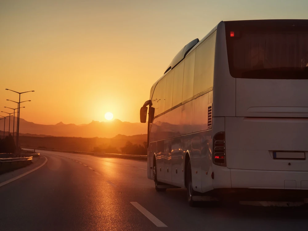White bus driving on road towards the setting sun