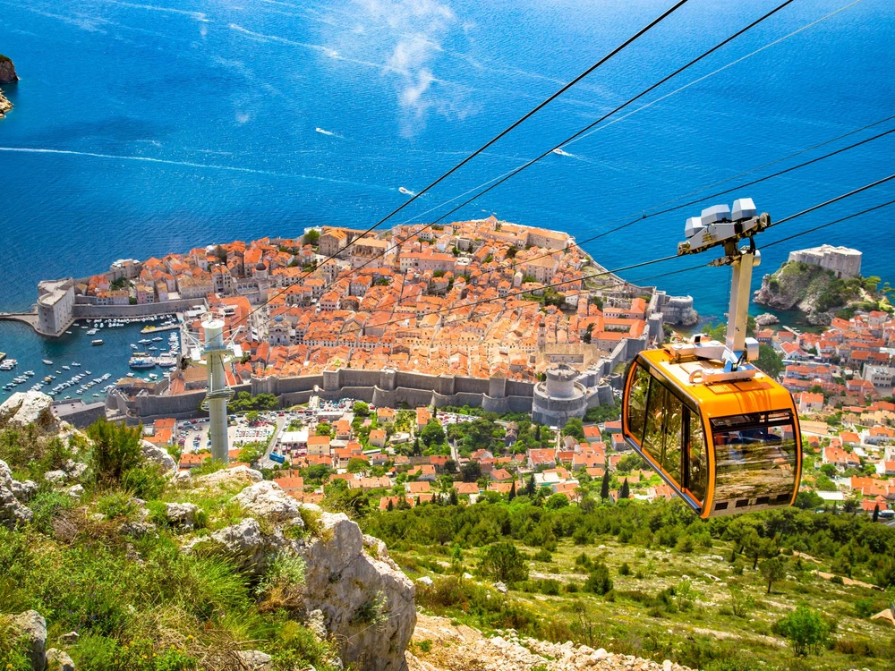 Aerial panoramic view of the old town of Dubrovnik with famous Cable Car on Srd mountain on a sunny day with blue sky and clouds in summer, Dalmatia, Croatia
