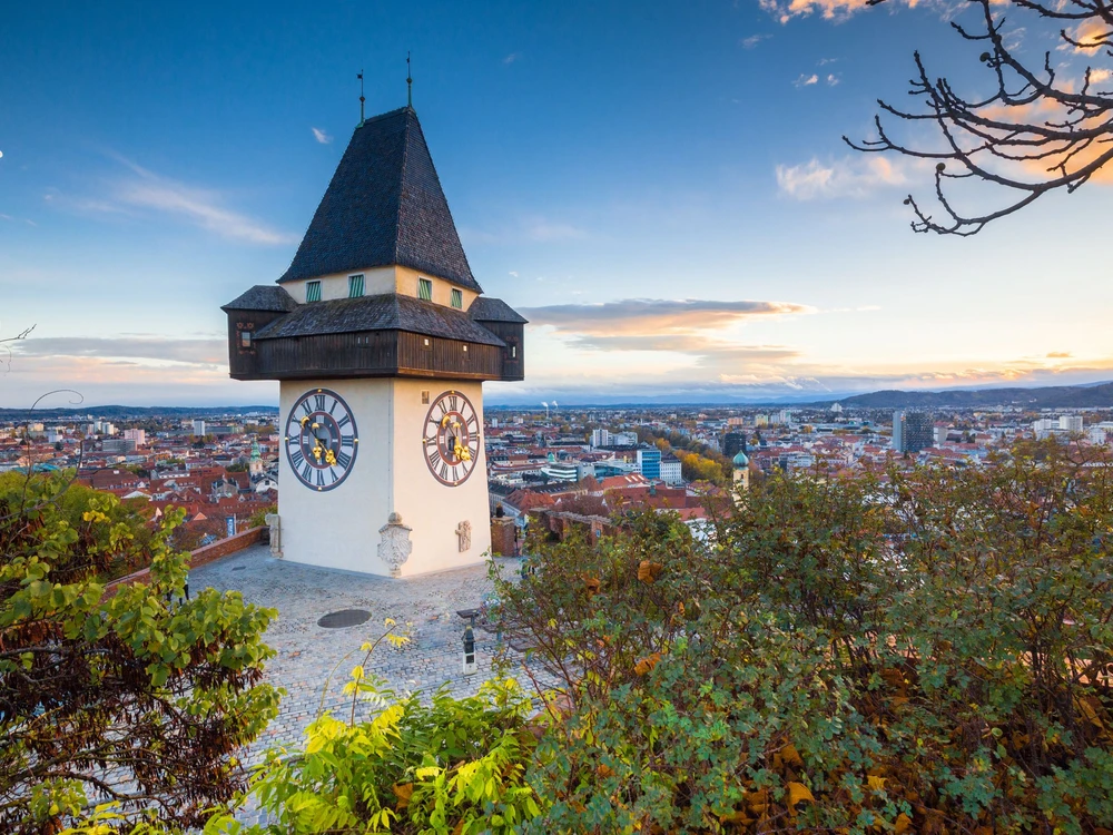 Classic panorama view of the historic city of Graz with famous Grazer Uhrturm clock tower in beautiful evening light at sunset, Styria, Austria