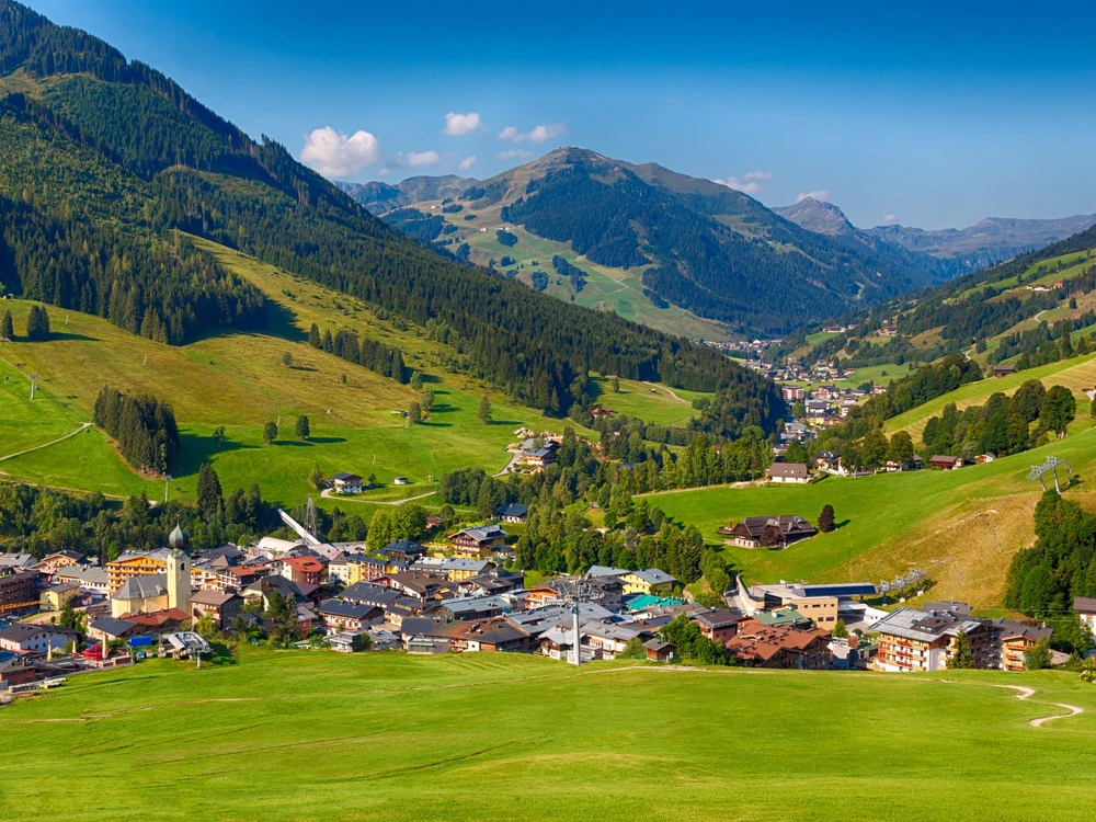 Beautiful view over the Austrian village Saalbach and some green fields in the Alps during summer.