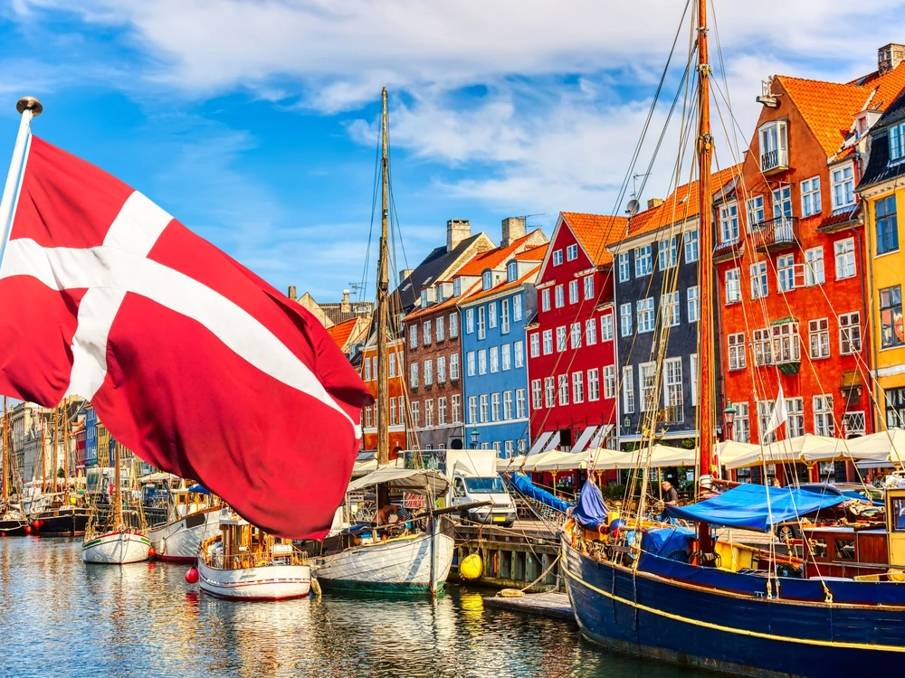 Copenhagen iconic view. Famous old Nyhavn port in the center of Copenhagen, Denmark during summer sunny day with Denmark flag on the foreground