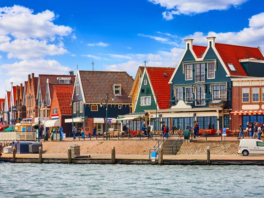 Volendam, Netherlands. Small town fishing village in North Holland near Amsterdam with traditional Houses with Red Tegular Roofs at Waterfront with Docks by Sea.
