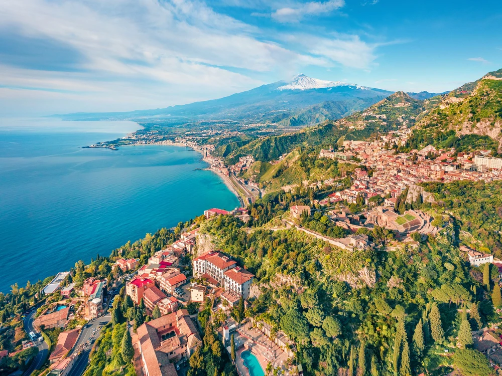 View from flying drone. Sunny morning view of Taormina town and Etna volcano on background. Nice spring seascape of Mediterranean sea. Splendid view of Sicily, Itale, Europe. Traveling concept background.