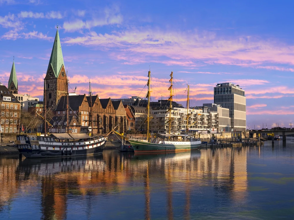 In der Dämmerung liegen Dreimaster vor der Promenade an der Weser in Bremen und spiegeln sich im Wasser