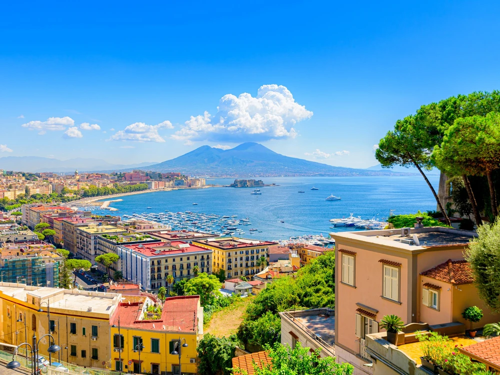Naples, Italy. View of the Gulf of Naples from the Posillipo hill with Mount Vesuvius far in the background and some pine trees in foreground. August 31, 2021.