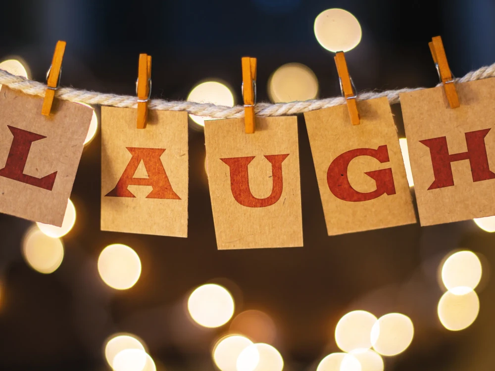 The word LAUGH printed on clothespin clipped cards in front of defocused glowing lights.