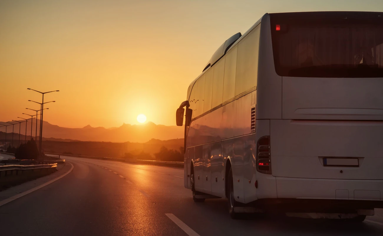 White bus driving on road towards the setting sun