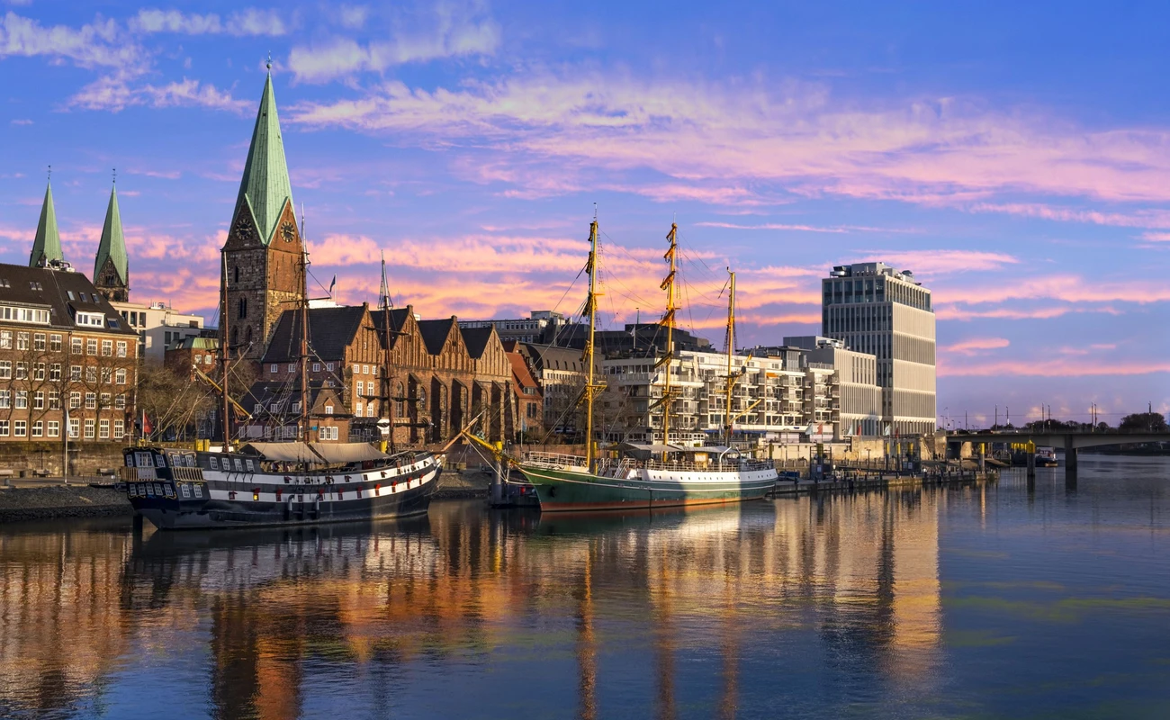 In der Dämmerung liegen Dreimaster vor der Promenade an der Weser in Bremen und spiegeln sich im Wasser