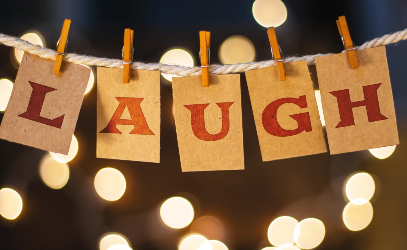 The word LAUGH printed on clothespin clipped cards in front of defocused glowing lights.